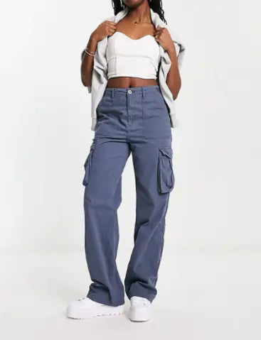 Woman wearing blue cargo pants with a crop top and jacket draped over her shoulders, standing against a plain white background.