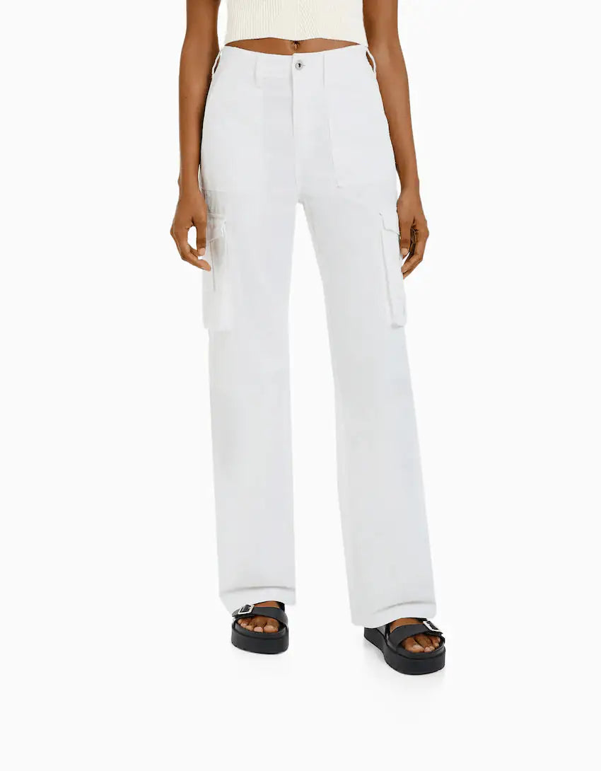 Front view of white utility cargo trousers with large side pockets and high-waist fit, worn with platform sandals.