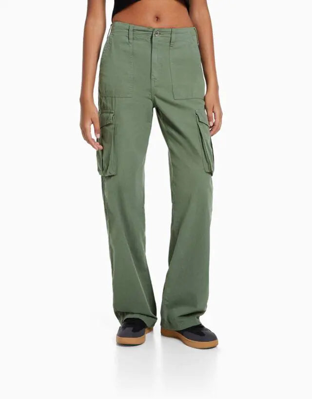 Front view of a woman wearing high-waisted olive green cargo trousers with flap side pockets, styled with a black crop top and black sneakers.