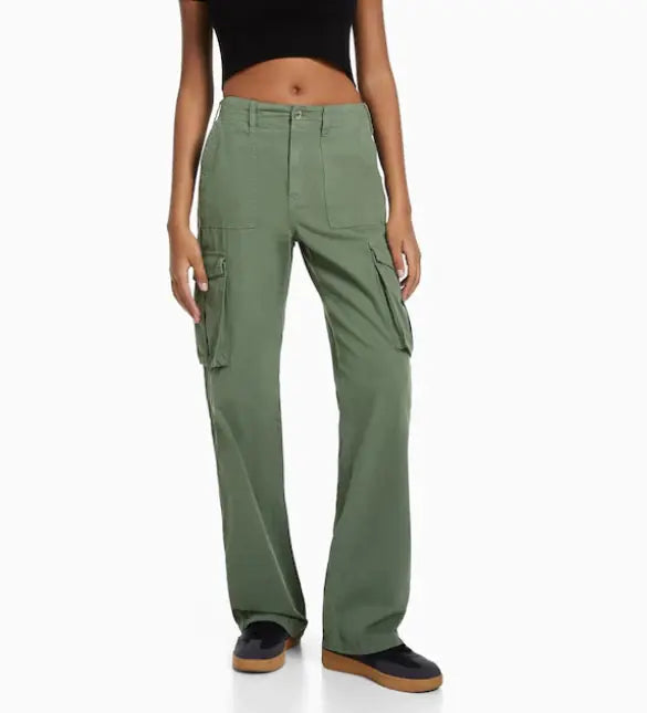 Front view of a woman wearing high-waisted olive green cargo trousers with flap side pockets, styled with a black crop top and black sneakers.
