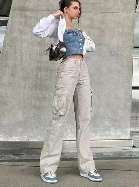 Woman in beige utility cargo trousers with flap pockets and a denim corset top, standing confidently against a concrete wall.