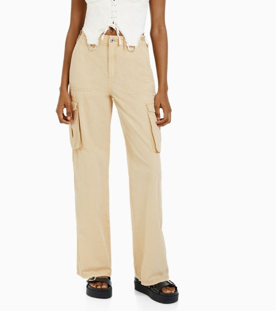Front view of beige high-waisted cargo trousers with flap side pockets, styled with a white cropped top and sandals.