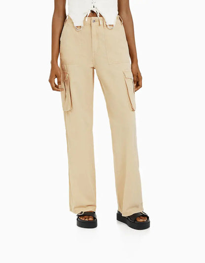 Front view of beige high-waisted cargo trousers with flap side pockets, styled with a white cropped top and sandals.