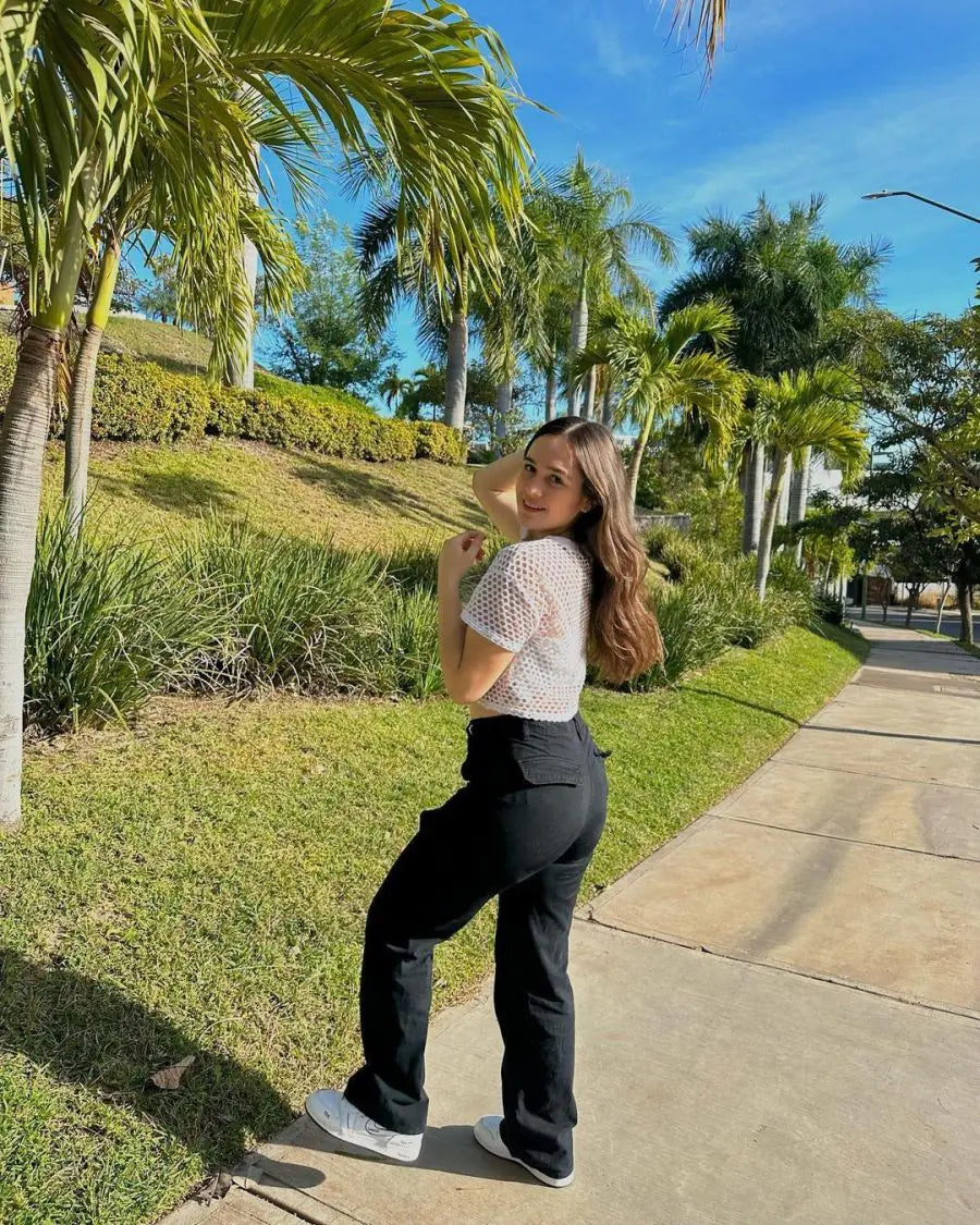 Woman in black cargo pants and white sneakers posing on a sunny sidewalk surrounded by palm trees.