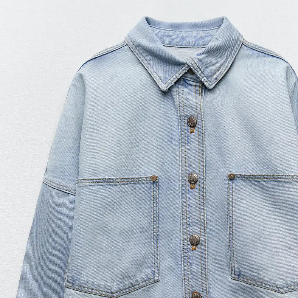 Close-up of front button and pocket details on light blue denim shirt jacket.