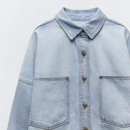 Close-up of front button and pocket details on light blue denim shirt jacket.
