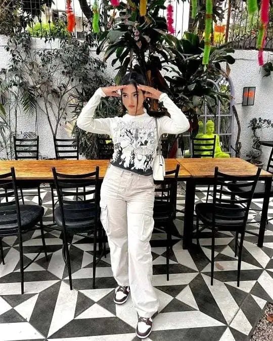 Woman posing indoors in beige wide-leg utility trousers and a printed long-sleeve top, standing in a modern café with geometric flooring.