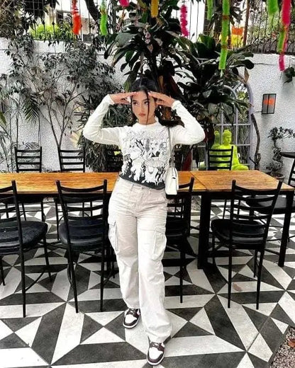 Woman posing indoors in beige wide-leg utility trousers and a printed long-sleeve top, standing in a modern café with geometric flooring.