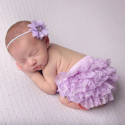 "Newborn baby sleeping in lavender lace bloomers with a matching flower headband on soft textured fabric"