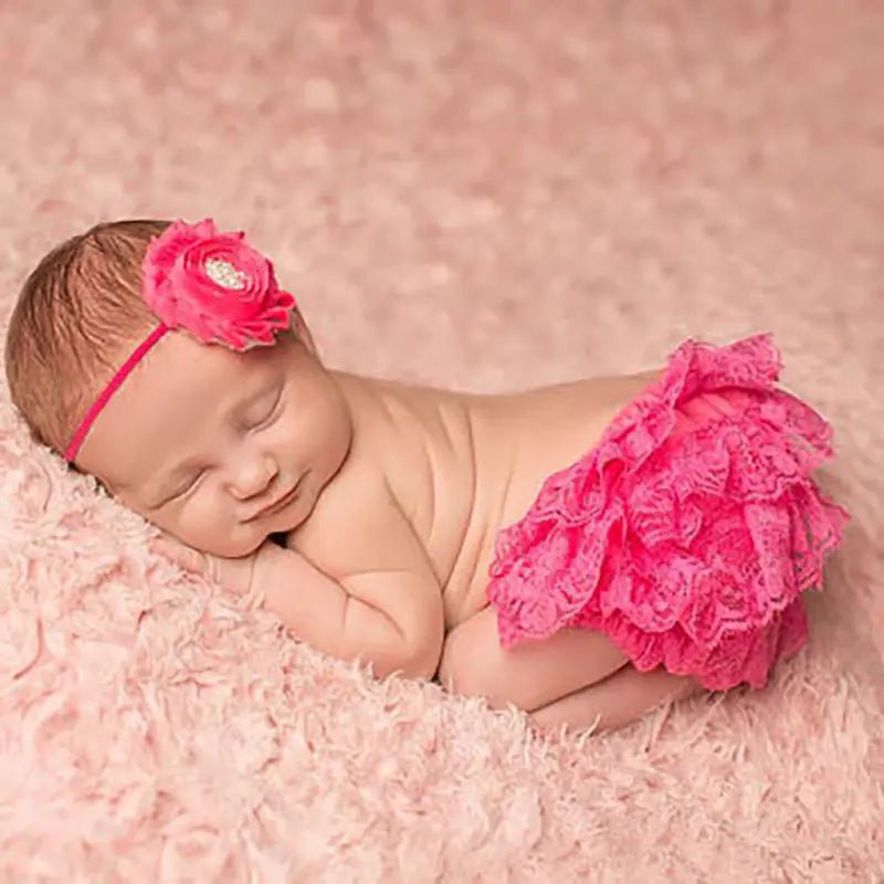 "Newborn baby in pink lace bloomers with matching flower headband resting on soft pink fabric"