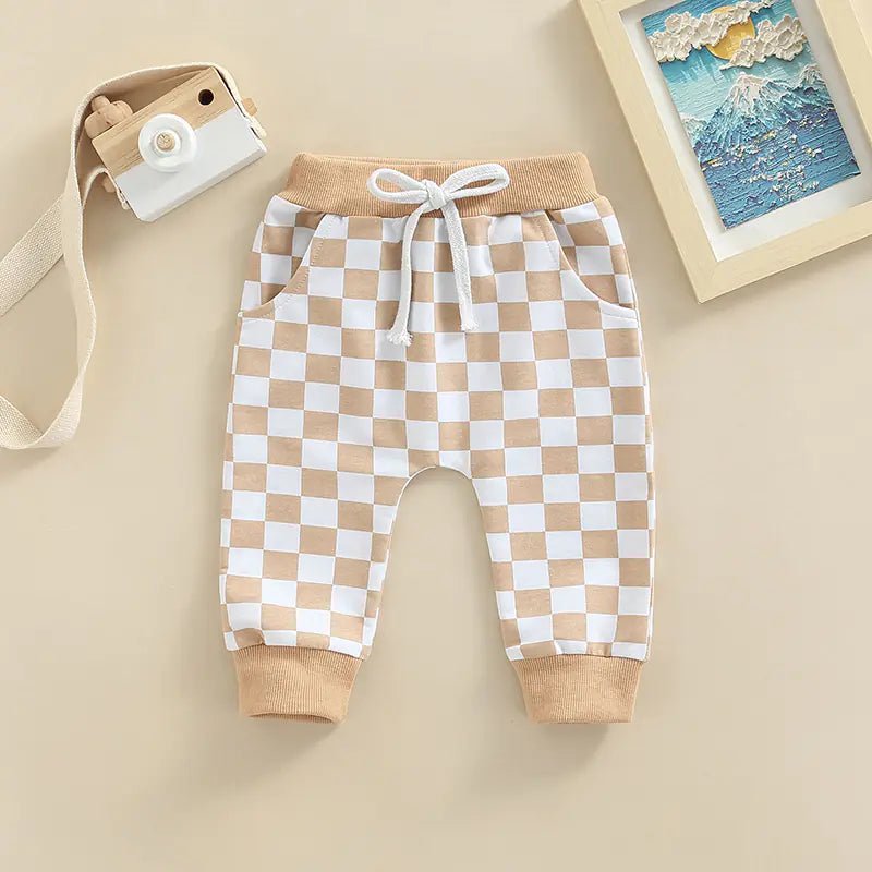Beige and white checkerboard baby pants with drawstring and ribbed cuffs, displayed flat on a beige background.