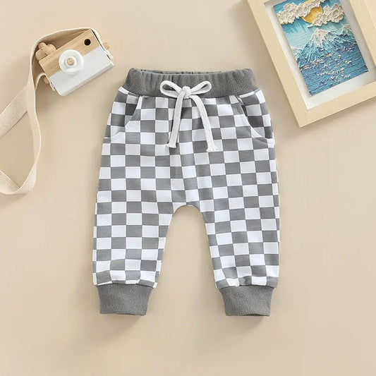 Gray and white checkerboard baby pants with drawstring and ribbed cuffs, displayed flat on a beige background.

