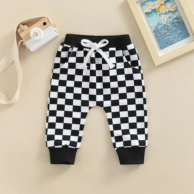 Gray and white checkerboard baby pants with drawstring and ribbed cuffs, displayed flat on a beige background.