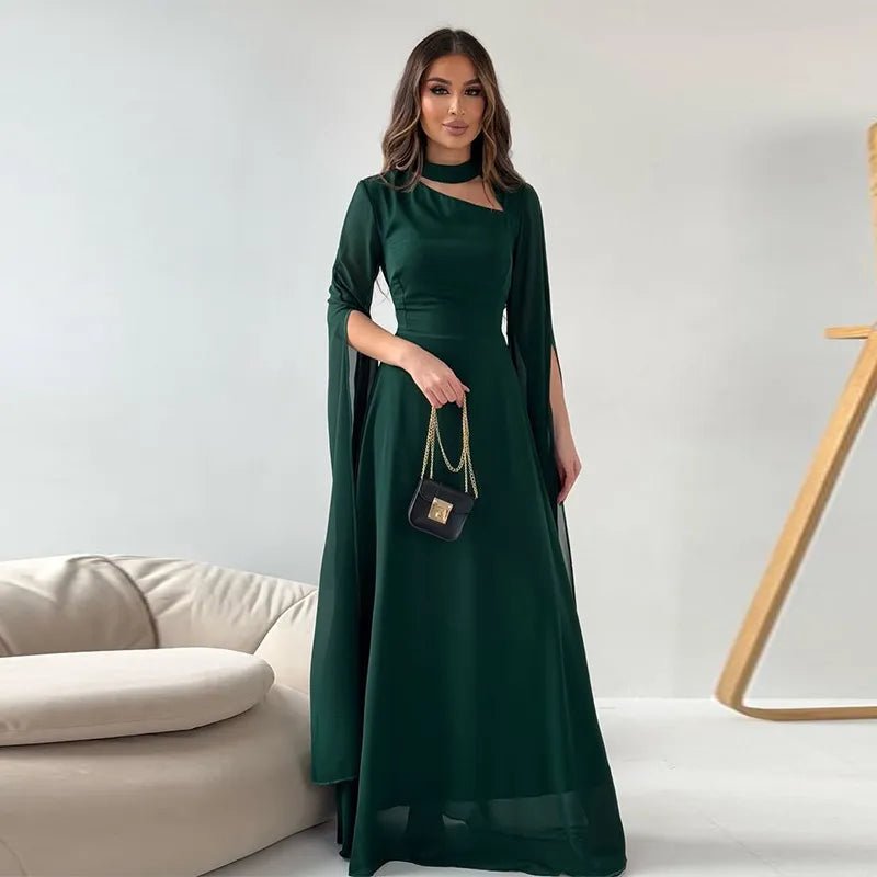 Elegant dark green women's evening gown with cape-style sleeves and choker neckline, paired with a small black handbag.