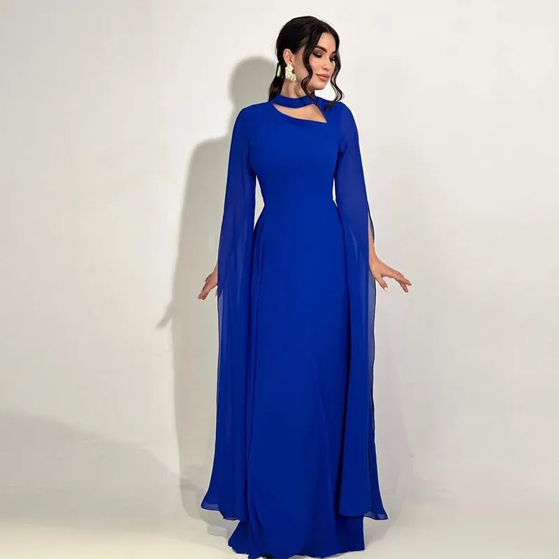 Woman in a royal blue elegant gown with a side cutout neckline and long chiffon cape sleeves, posing with both hands slightly lifted.