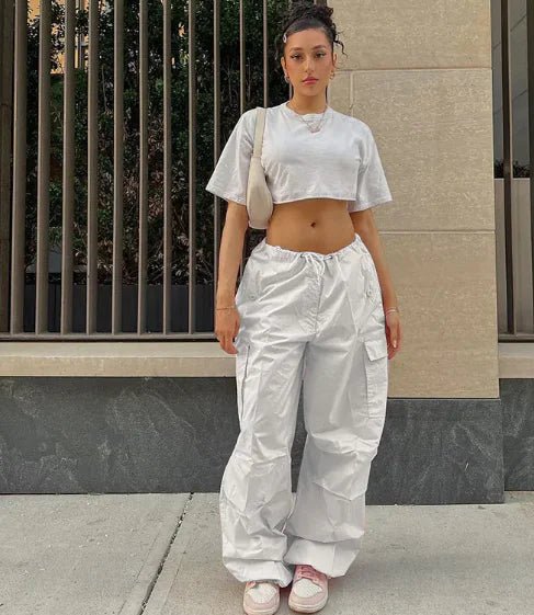 Woman wearing white high-waisted jogger pants and a cropped gray T-shirt, styled with pink sneakers and a beige shoulder bag.