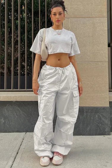 Woman wearing white high-waisted jogger pants and a cropped gray T-shirt, styled with pink sneakers and a beige shoulder bag.