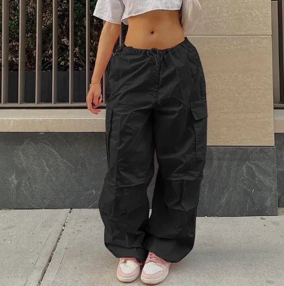 Woman wearing black high-waisted jogger pants and a cropped gray T-shirt, styled with pink sneakers and a beige shoulder bag.