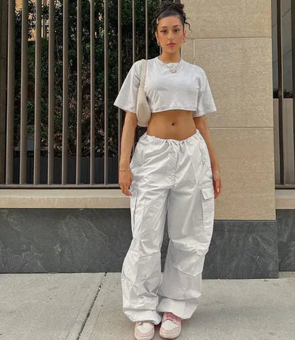 Woman wearing white high-waisted jogger pants and a cropped gray T-shirt, styled with pink sneakers and a beige shoulder bag.
