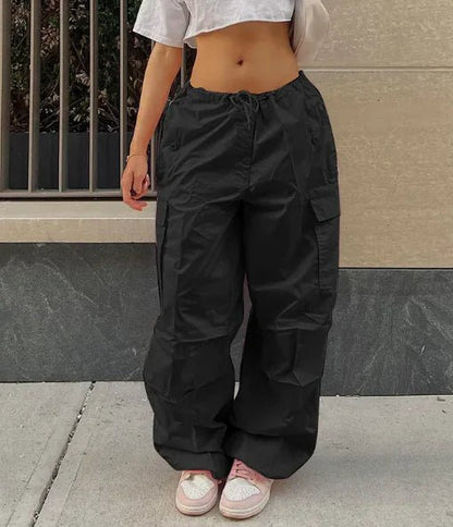 Woman wearing black high-waisted jogger pants and a cropped gray T-shirt, styled with pink sneakers and a beige shoulder bag.