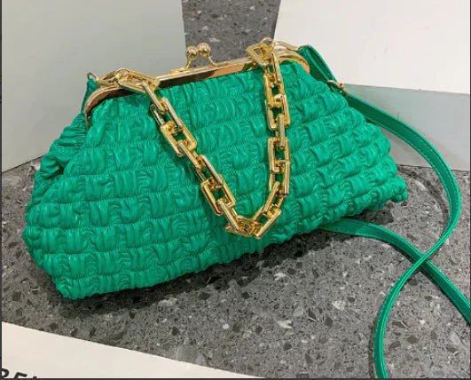 Green pleated handbag with chain strap placed on grey stone.