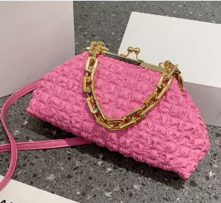 Pink pleated handbag with gold chain strap placed on grey countertop.