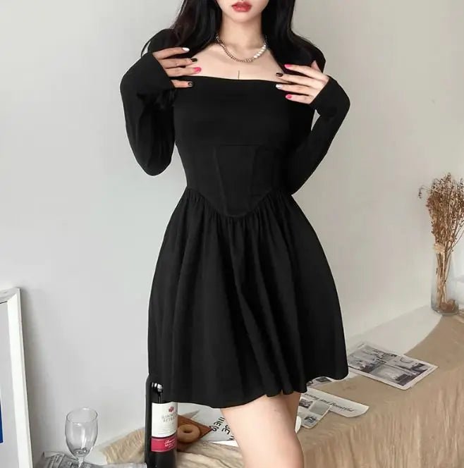 Front View: Woman wearing a black square neck mini dress with long sleeves, fitted bodice, and flared skirt, standing indoors beside a wine bottle.
