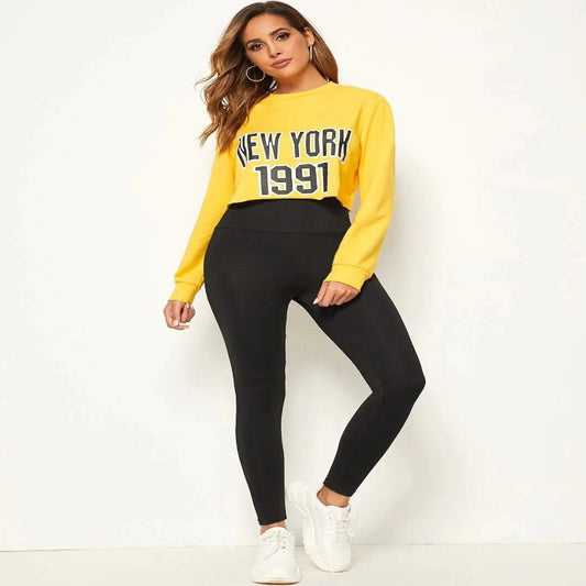 Woman wearing a yellow sweatshirt with 'New York 1991' print and black leggings, perfect for yoga, sports, or casual wear."

