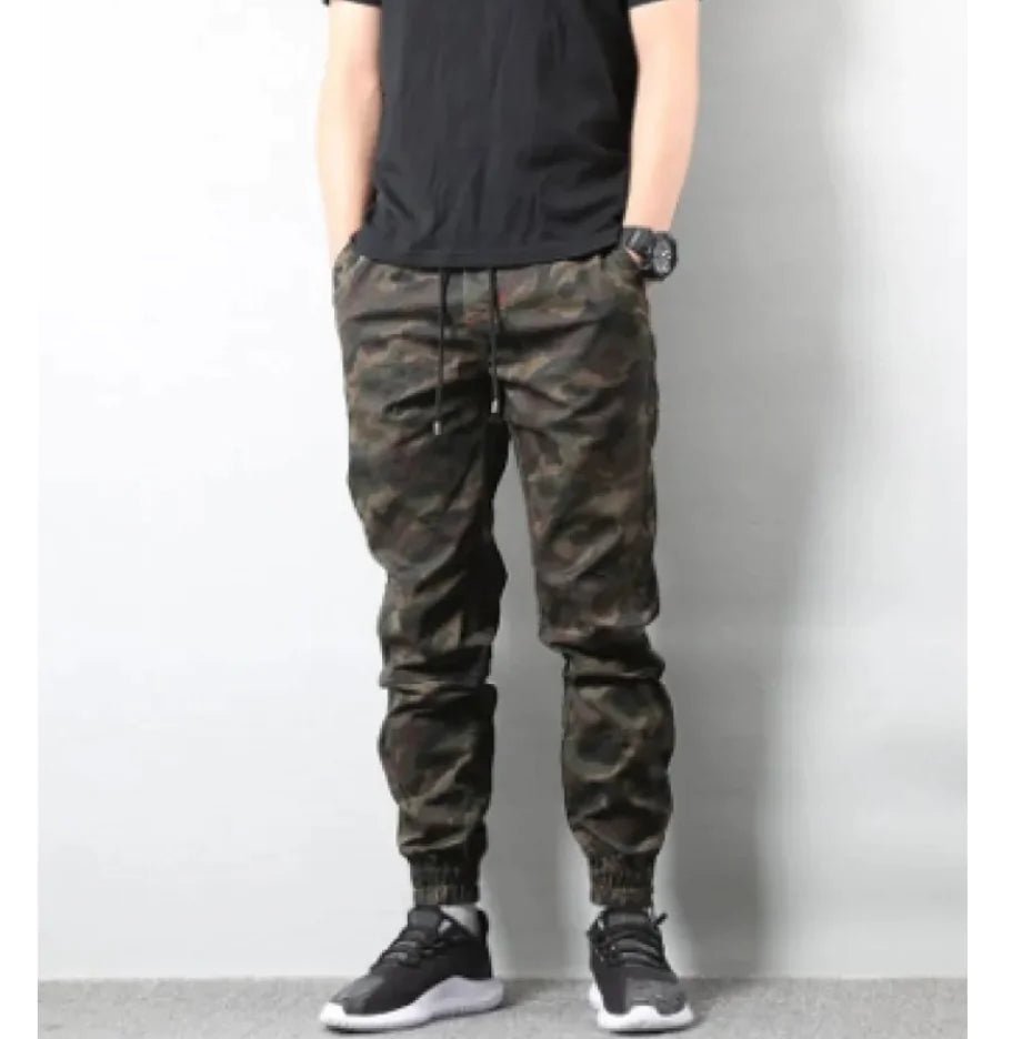 Man wearing retro camouflage jogger pants with drawstring waist and elastic cuffs, standing with hands in pockets.