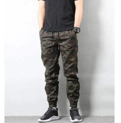 Man wearing retro camouflage jogger pants with drawstring waist and elastic cuffs, standing with hands in pockets.
