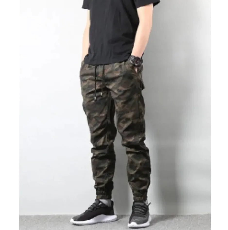 Man wearing retro camouflage jogger pants with drawstring waist and elastic cuffs, standing with hands in pockets.