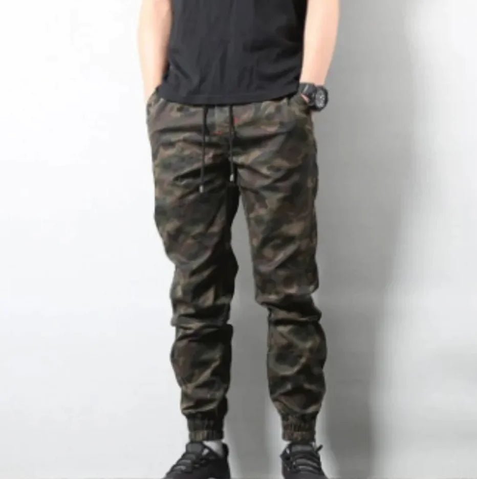 Man wearing retro camouflage jogger pants with drawstring waist and elastic cuffs, standing with hands in pockets.