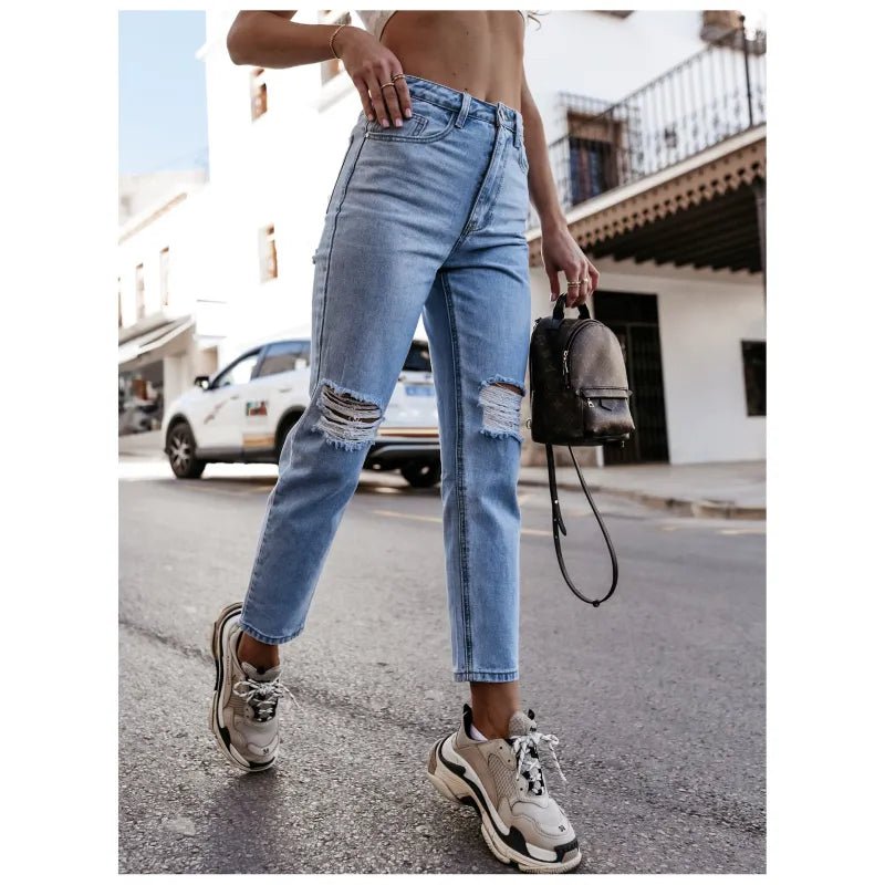High-waisted ripped jeans in classic blue, styled with sneakers and a crop top, captured outdoors for a casual urban look.