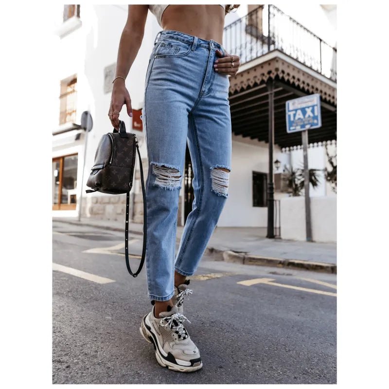 High-waisted ripped jeans in classic blue, styled with sneakers and a crop top, captured outdoors for a casual urban look.