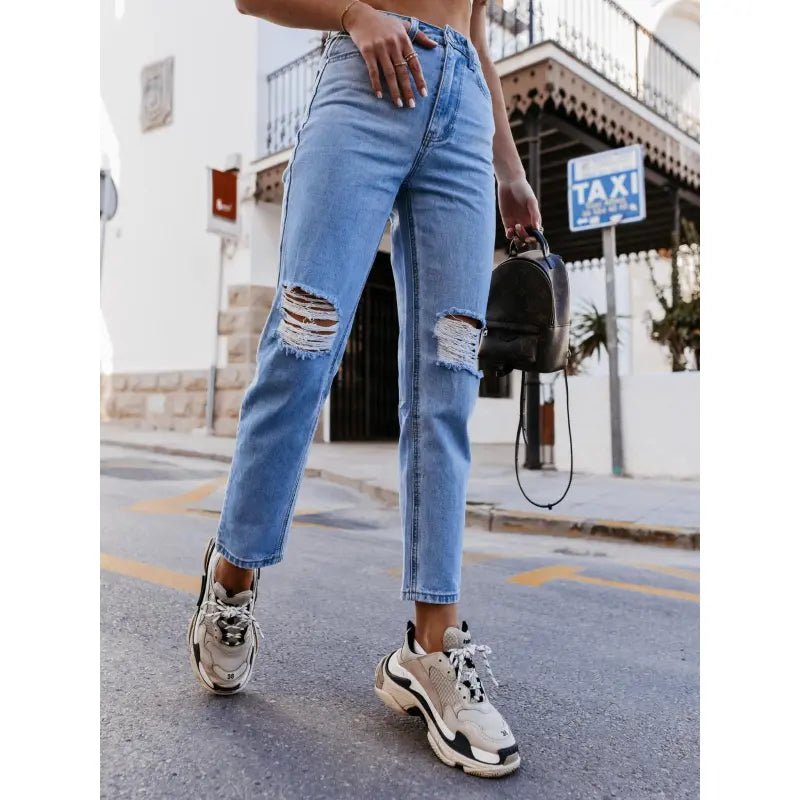 High-waisted ripped jeans in classic blue, styled with sneakers and a crop top, captured outdoors for a casual urban look.