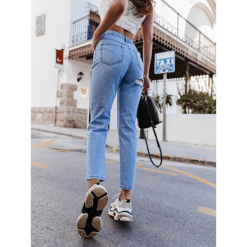 Back view of high-rise straight-leg blue jeans with a subtle distressed detail, styled with sneakers and a casual crop top in a city street setting.