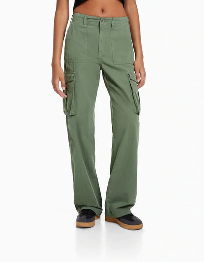 Front view of a woman wearing high-waisted olive green cargo trousers with flap side pockets, styled with a black crop top and black sneakers.