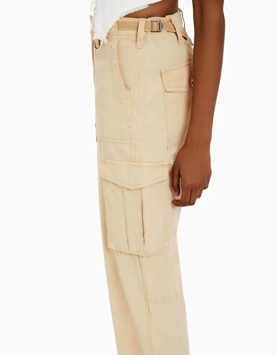 Side view of beige high-waisted cargo trousers with flap side pockets, styled with a white cropped top and sandals.