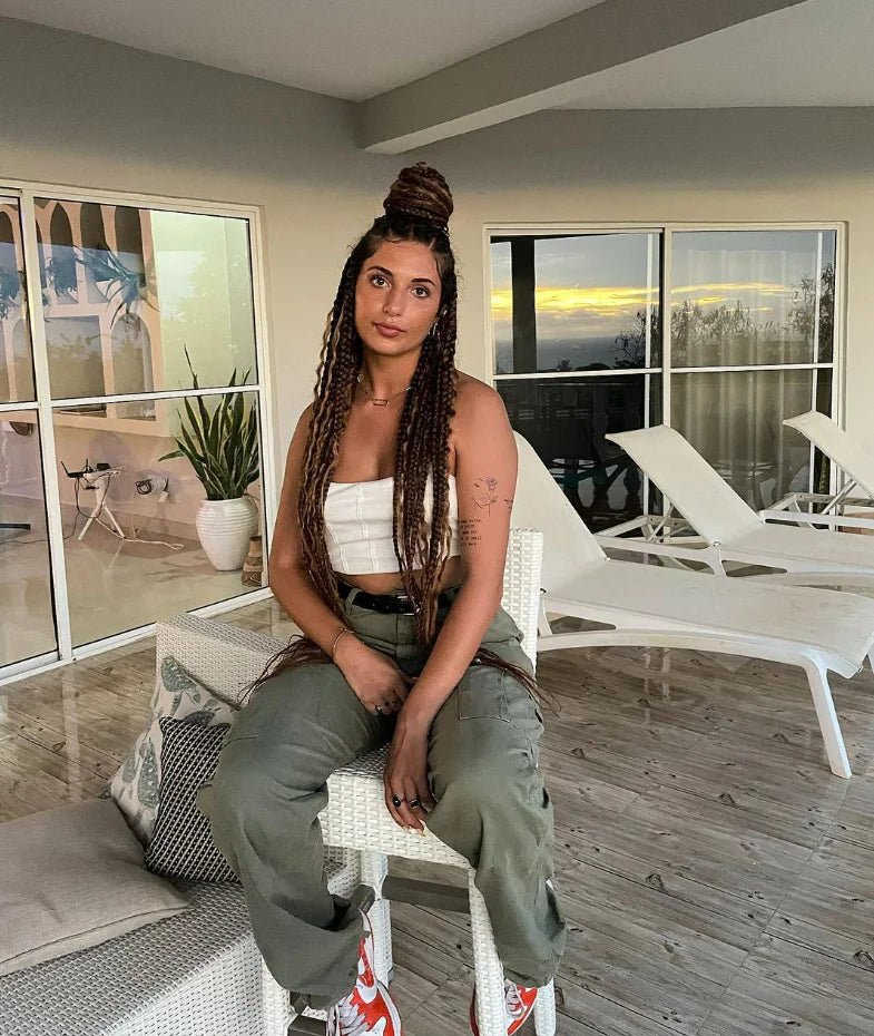 Woman sitting on a patio chair wearing olive green cargo pants and a white top, with a sunset view behind her.